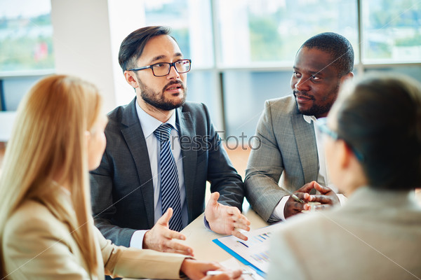 Serious businessman of Asian ethnicity speaking while his colleagues listening to him at meeting, stock photo