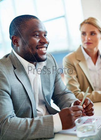 African businessman sitting at workplace in office on background of female colleague