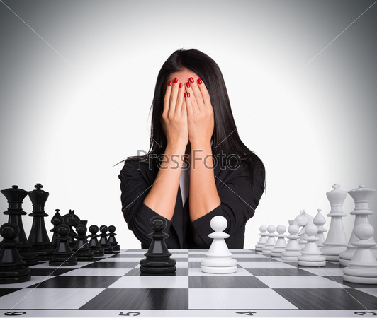 Businesswoman covering her face with hands. Chessboard with chess. Gray background. Business concept