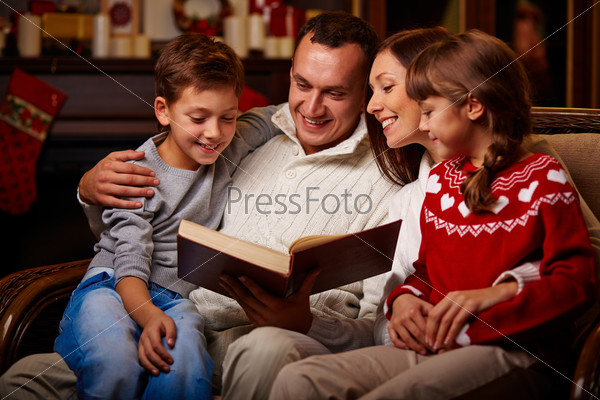 Cheerful family of four reading together on Christmas evening