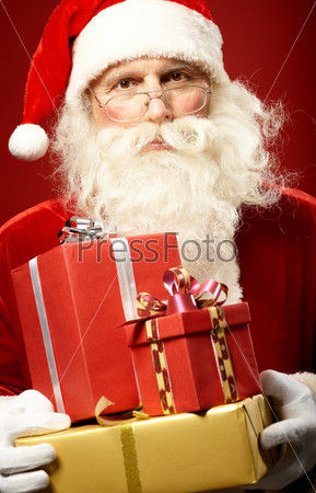Serious Santa Claus with giftboxes looking at camera