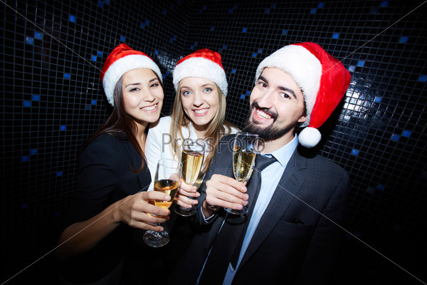 Group of cheerful business people in Santa caps toasting with champagne in nightclub