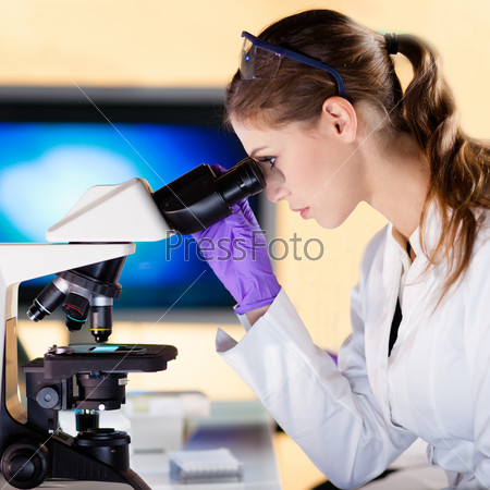 Attractive young scientist looking at the microscope slide in the forensic laboratory.
