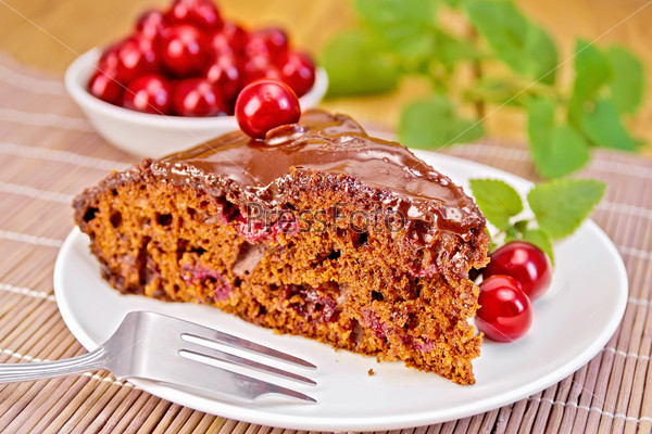 Chocolate cake with cherries on a plate, cherries, mint on a bamboo napkin on the background of wooden boards