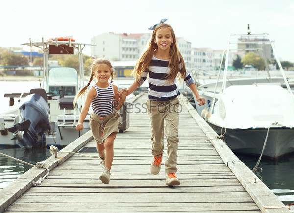 Two fashion kid girls wearing navy clothes in marine style walking in the sea port