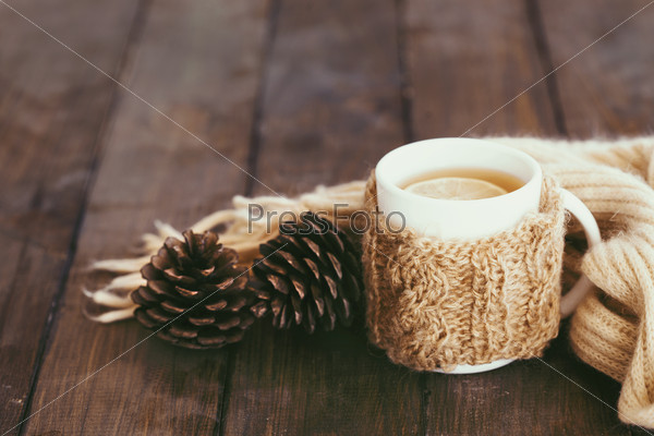 Cup of hot tea with lemon dressed in knitted warm winter scarf on brown wooden tabletop