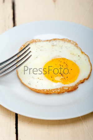 fried egg sunny side up on a plate with fork over wood table