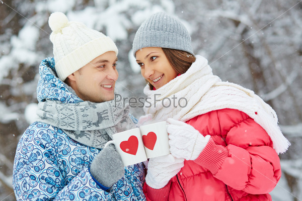 Portrait of happy young couple cheering up with drinks in winter park