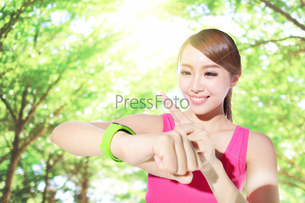 Health sport woman wearing smart watch device with touchscreen doing exercises with green tree background, asian