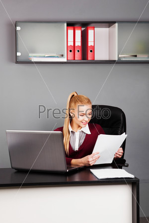businesswoman sitting at workplace and reading paper in office