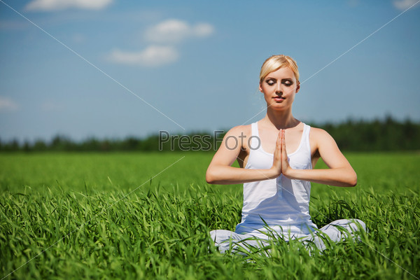 Beautiful young woman doing yoga exercise on field. Yoga concept.
