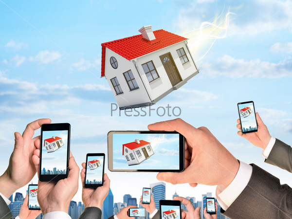 Hands holding smart phones and shoot video as falling house. City on background, stock photo