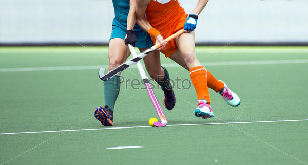 Two field hockey player, fighting for the ball on the midfield during an intense match on artificial grass