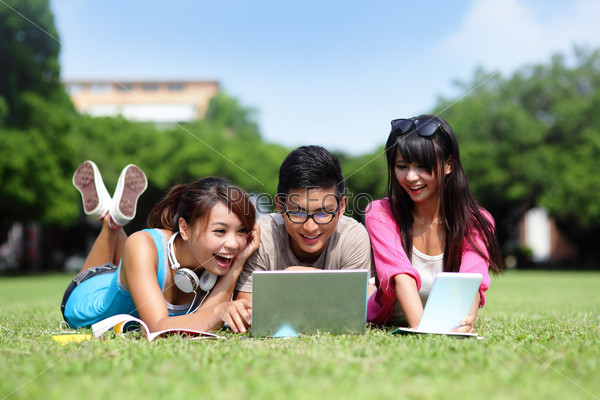 Happy College students using laptop and tablet pc on campus lawn, asian
