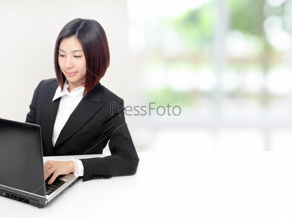 Young Business woman using computer and sit at company office with white table, window outside are green background, model is a asian beauty