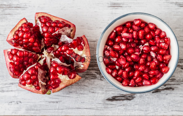 Half pomegranate and pomegranate seeds on a white wooden background