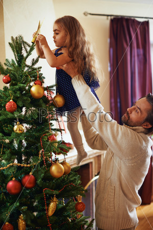 Man in white sweater helping his daughter to decorate Christmas tree