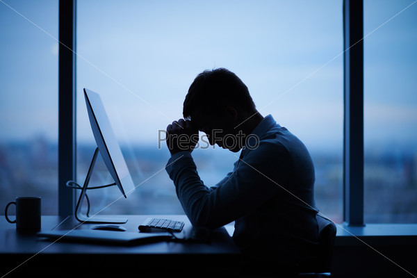 Tired or stressed businessman sitting in front of computer in office, stock photo