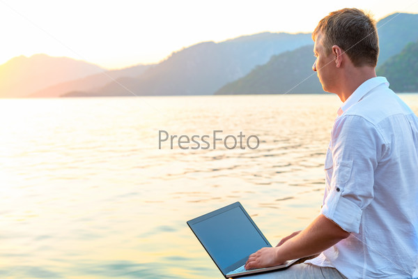 Мужчина с ноутбуком на берегу
