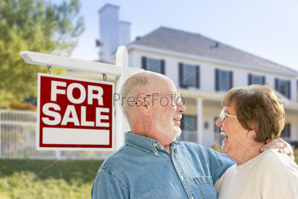 Happy Senior Couple Front of For Sale Real Estate Sign and House.
