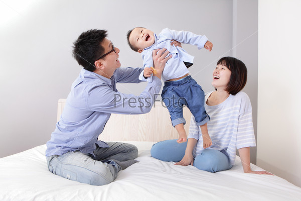 happy father hug his son with smile mother sitting on bed at home, asian family