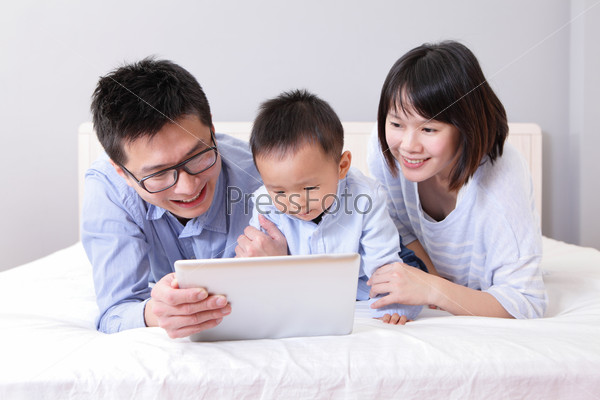 cute boy using tablet pc with A happy, family of mother, father, lying on bed at home, asian people