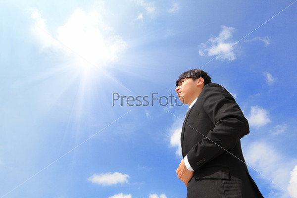 Successful business man standing over blue sky and\
purposefully looking away.