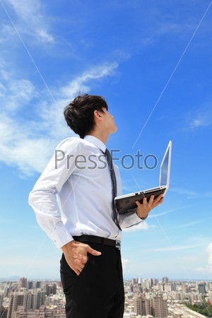 Young business man using laptop and look to blue sky and cloud with cityscape in the background, business and cloud computing concept