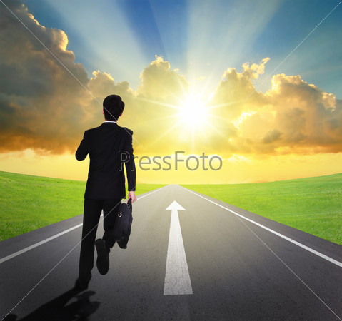 business man running forward on asphalt road with arrow , and\
beautiful sunset and sunshine, business concept