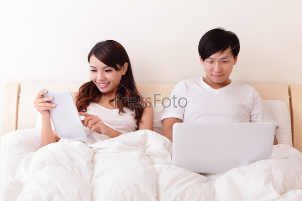 Cheerful couple using touch pad in bed