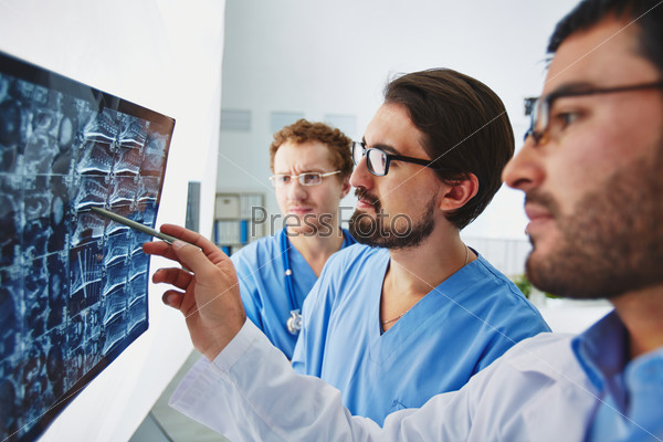 Young male doctor pointing at x-ray and discussing it with colleagues, stock photo