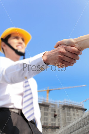 Worker and architect shaking hands at construction site comparing housing project with building