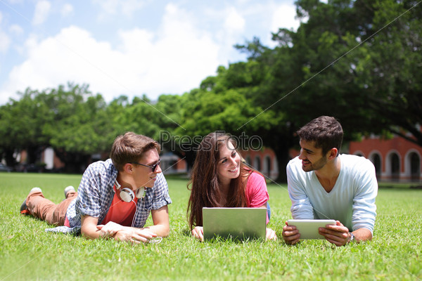 Happy College students using laptop and tablet pc on campus lawn, caucasian