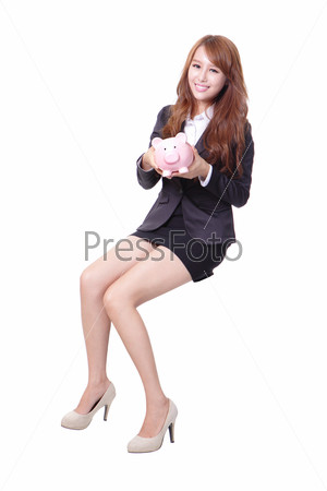 Happy business woman holding pink piggy bank and sitting on\
something isolated against white background, asian beauty