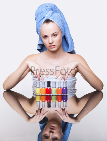 Young pretty spa woman in blue bath towel on head with nail varnish over mirror table on white background