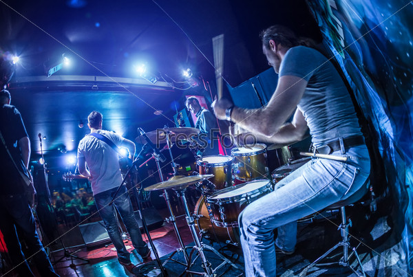 Drummer playing on drum set on stage. Warning - Focus on the drum, authentic shooting with high iso in challenging lighting conditions. A little bit grain and blurred motion effects, stock photo
