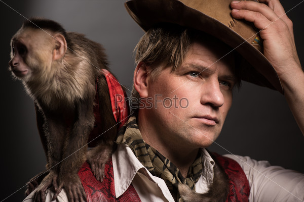 Mature man adventurer in costume of traveler with his monkey companion on black background