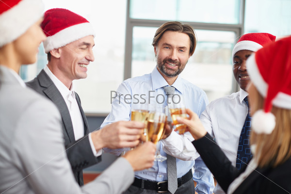 Friendly business partners in Santa caps toasting with champagne at corporate party