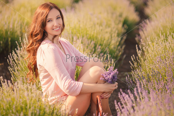 Beautiful sexy caucasian woman sitting on the grass on summer meadow. Portrait of the young beautiful smiling woman outdoors.
