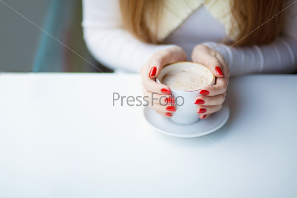 Woman\'s hands hugging a cup of coffee in a restaurant