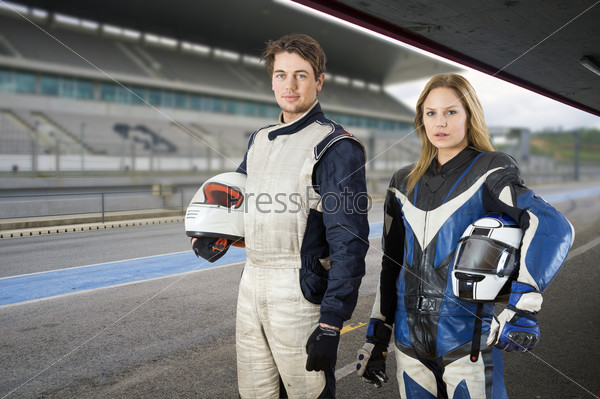 Motor cyclist and a race car driver posing in the pit box in front of the grand stand of a race track