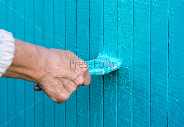 Hand with a paint brush paints wooden wall