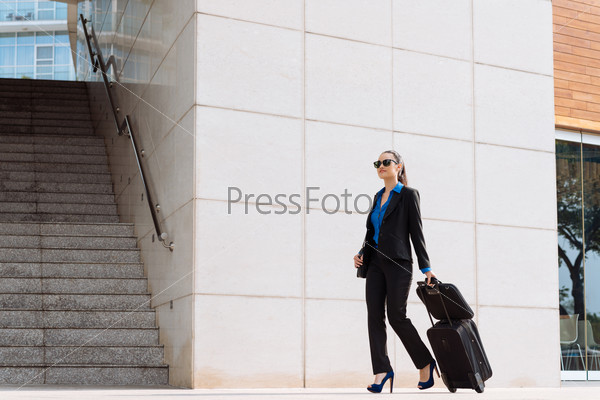 Stylish business woman with luggage walking along the street