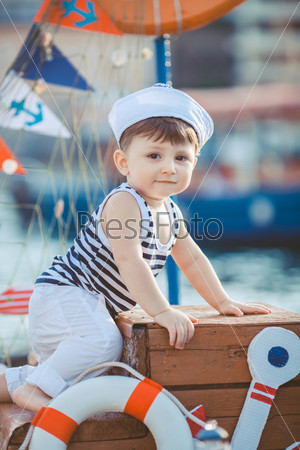 cute little boy sitting on the floor on pier outdoor, a marine style. Little sailor