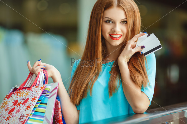 Young woman with credit card and shopping bags. Portrait of a young woman holding shopping bags and a credit card. Young woman with shopping bag and card in store