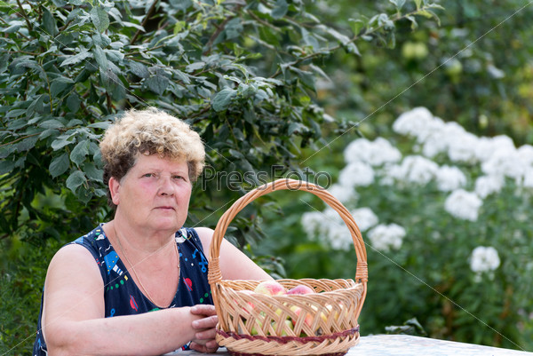 An elderly woman with a basket of apples in the garden