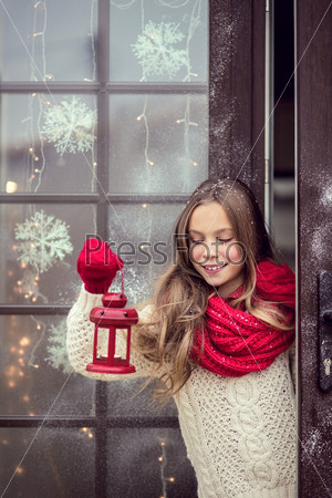 Child girl welcome guests and holding holiday lantern, snow weather, house is decorated before Christmas