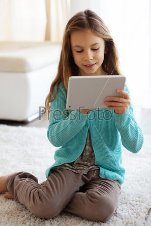 Child playing on ipad tablet pc sitting on a carpet at home