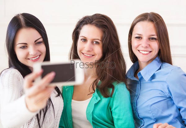 Three smiling teenage girls taking selfie with smartphone camera at home. Friendship, technology and internet concept
