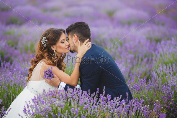 Young couple in love bride and groom, wedding day in summer. Enjoy a moment of happiness and love in a lavender field. Bride in a luxurious wedding dress.